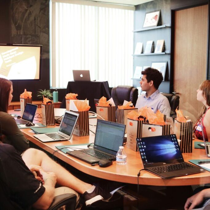 A group of people at a meeting around a table, they all have laptops